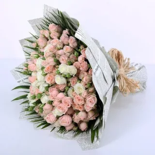 Bouquet of soft peach and white spray roses, accented with palm leaves, wrapped in newspaper and tied with raffia.