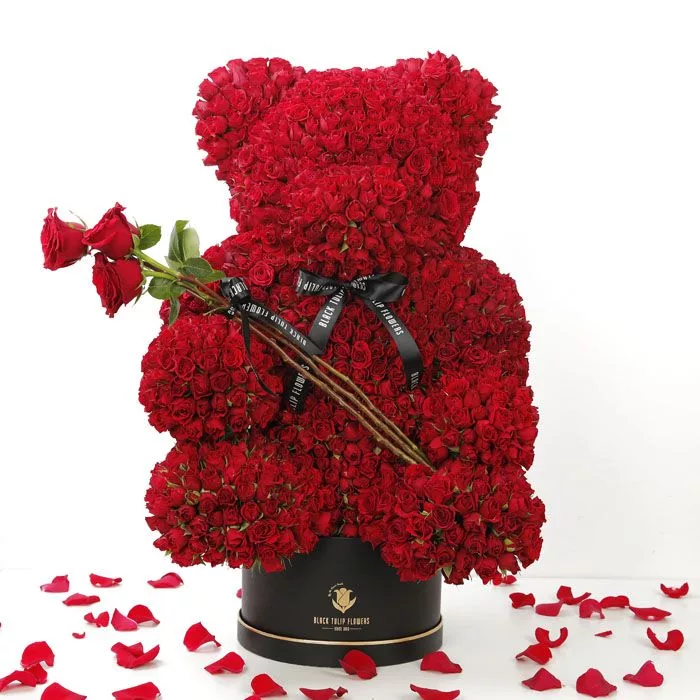 Teddy-shaped arrangement of 100–150 red spray roses, 3 hand-tied roses with black ribbon, in a black round box.