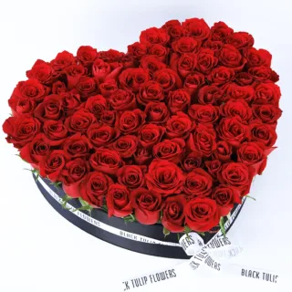 A heart-shaped black box filled with 80-100 exquisite red roses, elegantly adorned with a white ribbon.