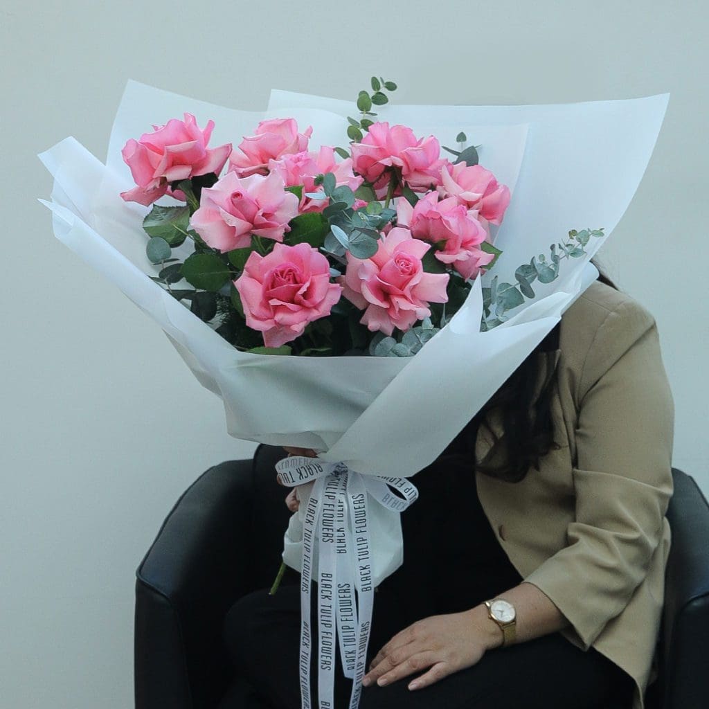 1923 Bouquet featuring 10 delicate pink roses paired with eucalyptus, wrapped in a white covering and tied with a white ribbon.