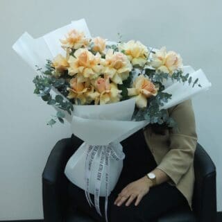 BTF Home 18 A bouquet of delicate peach roses and fresh eucalyptus, elegantly wrapped in white and tied with a matching white ribbon.