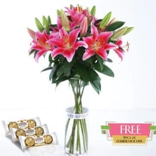 A bunch of pink lilies in a glass vase, accompanied by a box of Ferrero Rocher chocolates.