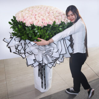 A large, elegant arrangement of 300 peach roses with added greenery wrapped in white and tied with a black ribbon.