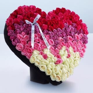 180-200 mix coloured roses arranged in a heart shape, adorned with a white ribbon.