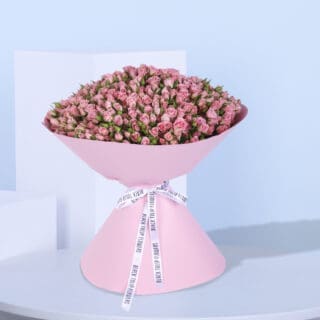 A large bouquet of 100 pink spray roses wrapped in pink paper with a white ribbon.
