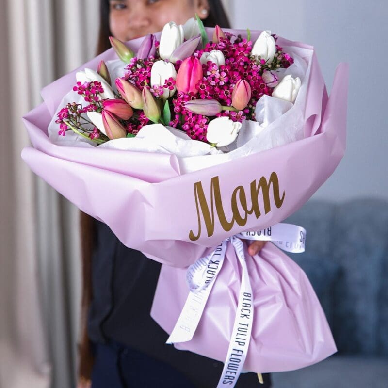 For You Mom Bouquet (1) A person holding a beautifully wrapped bouquet of pink and purple tulips, with "MOM" elegantly printed on the wrapping