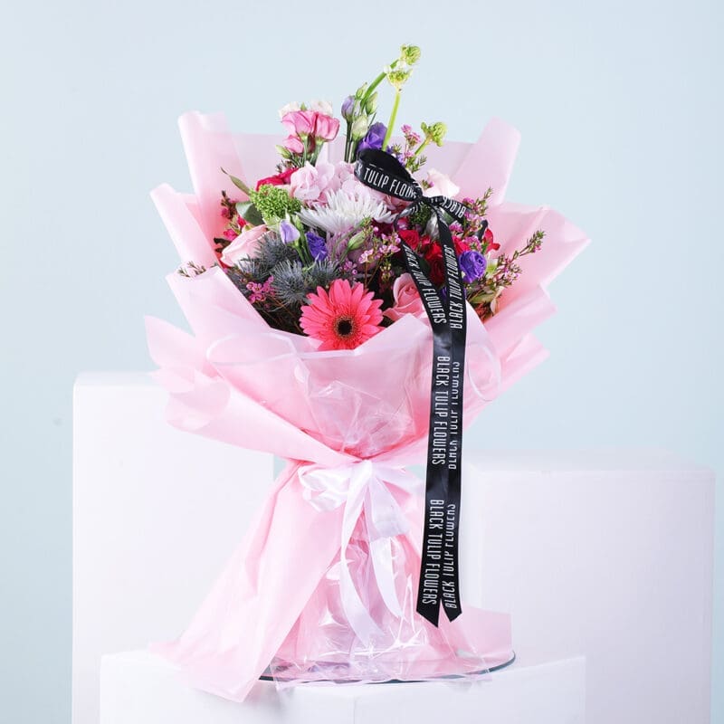 01 A colorful mixed flower bouquet wrapped in pink tissue paper and tied with a black ribbon featuring the Black Tulip Flowers