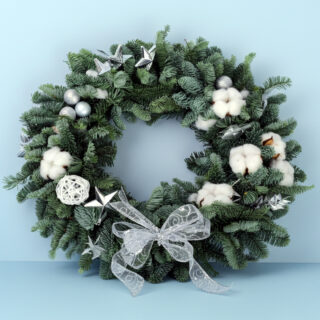 A festive Christmas wreath adorned with green pine leaves, decorative ornaments, and fluffy cotton flowers.