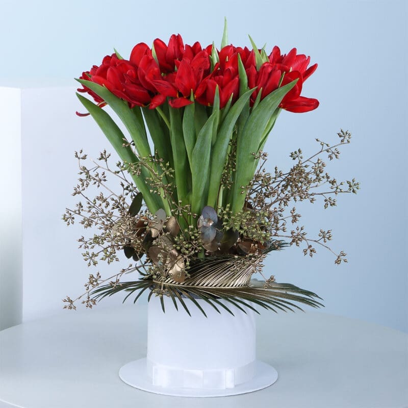 A bouquet of red tulips in a white vase with golden leaves and branches