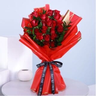 A bouquet of a dozen red roses wrapped in red tied with a black ribbon.