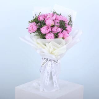 A bouquet of pink peonies wrapped in white paper, tied with a ribbon.