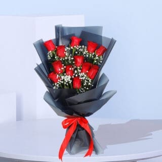 A bouquet of a dozen red roses surrounded by baby's breath, wrapped in black paper and tied with a red ribbon.
