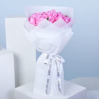 A bouquet of pink peonies wrapped in white paper, tied with a white ribbon.
