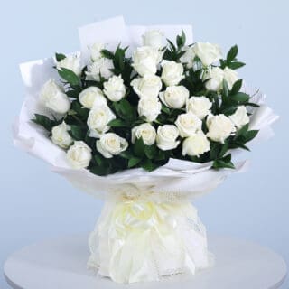 Bouquet of 30 white roses with fresh green leaves in a white wrap and tied with a white ribbon.