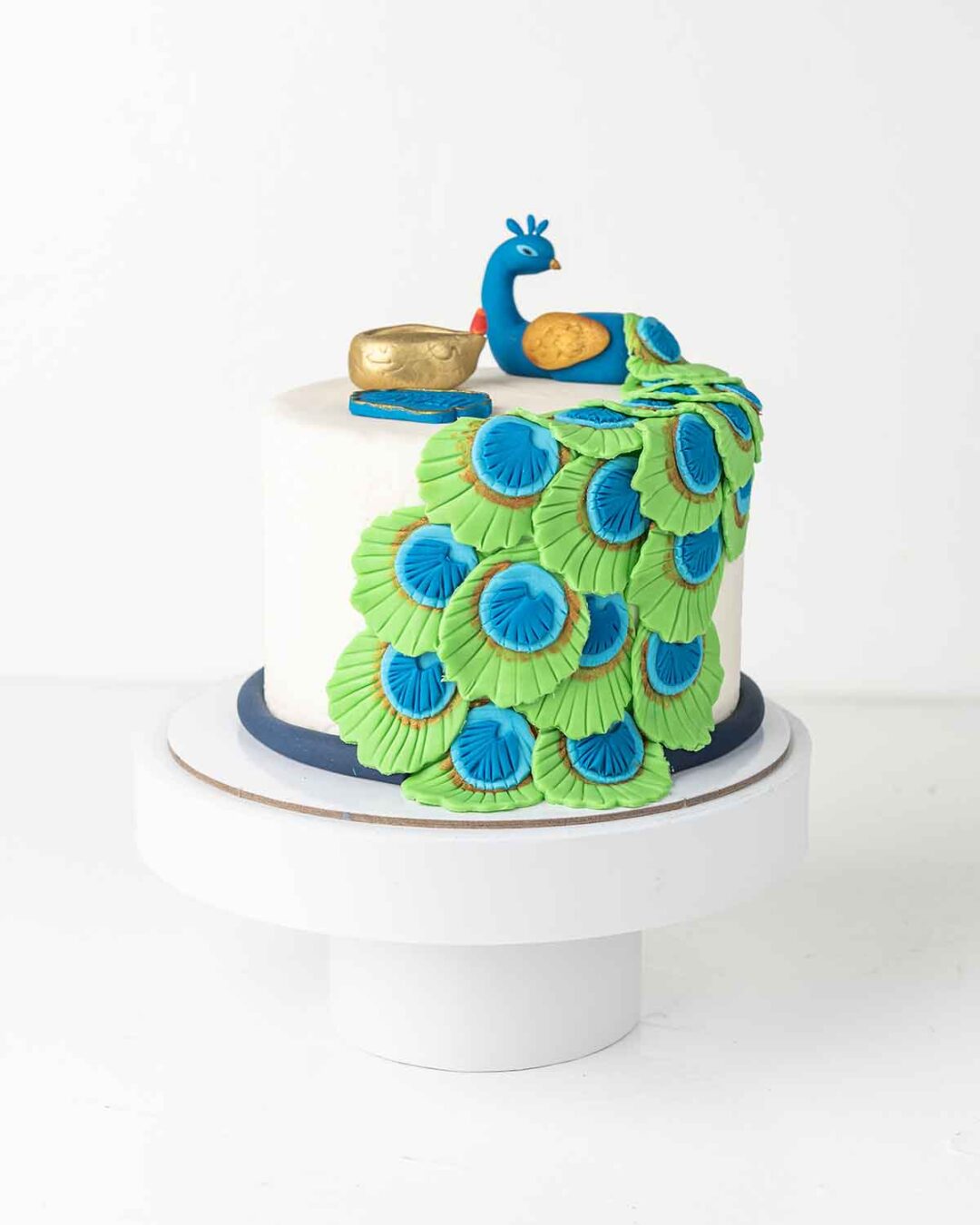 A white cake decorated with a blue and green peacock, a golden diya, and a sign that says "Happy Diwali.