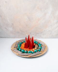 A Diwali platter filled with colorful treats and decorations. There are red candles in the center, surrounded by silver-dipped almonds, orange and green candies, and other festive snacks.