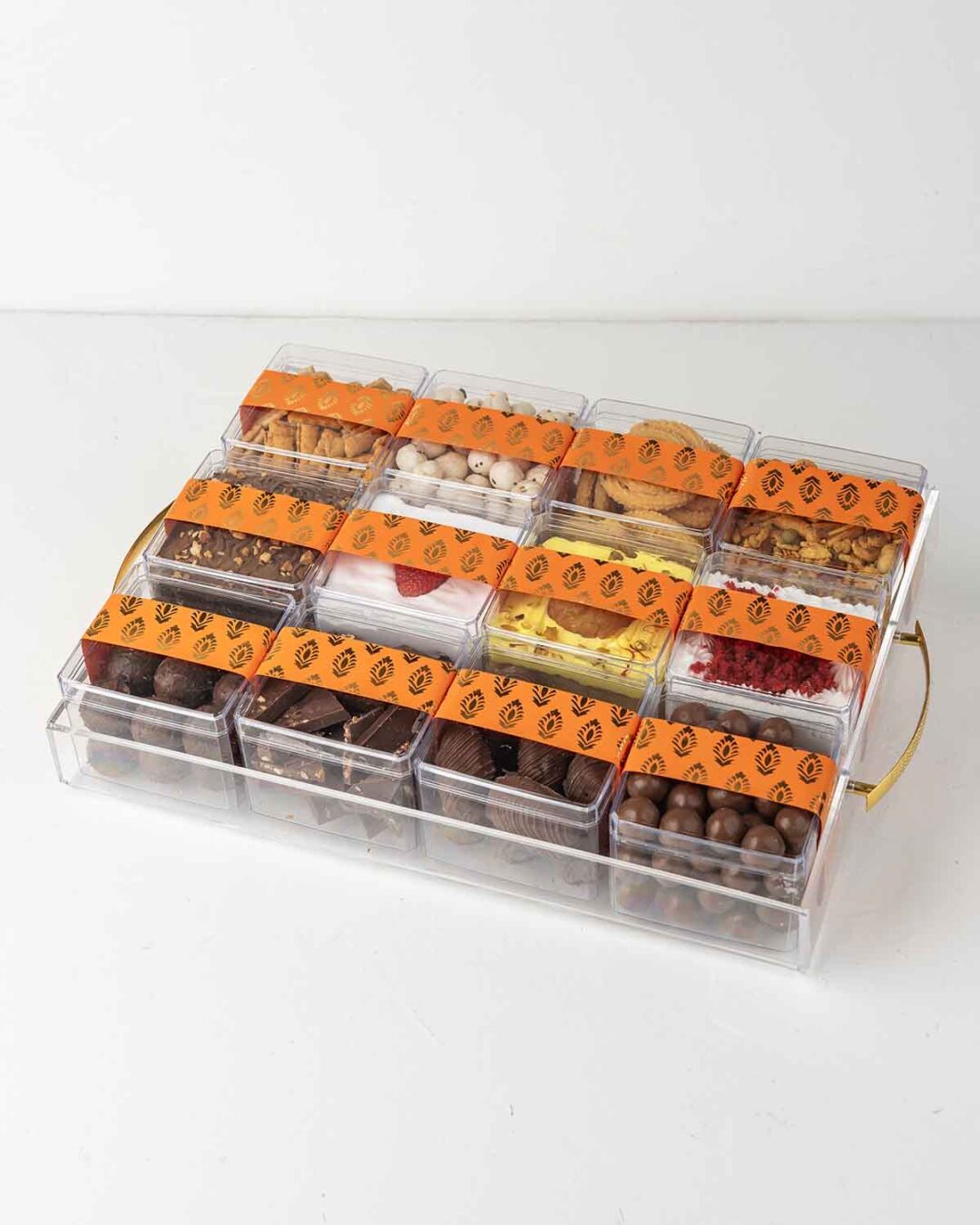 A transparent gift tray filled with assorted treats like cakes, truffles, and snacks for Diwali.