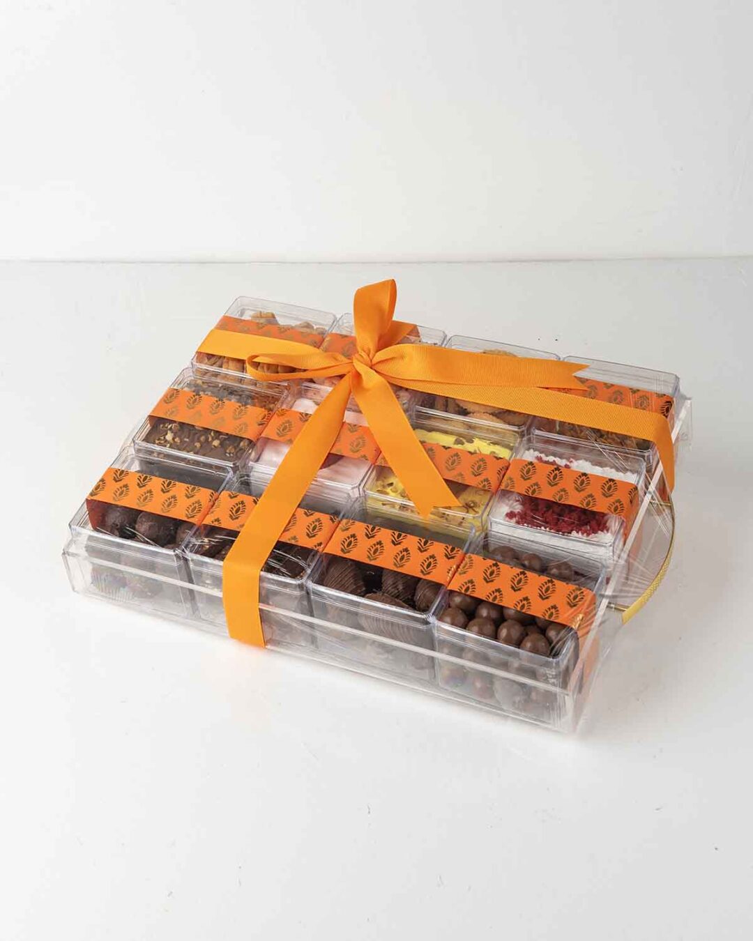 A transparent gift tray filled with assorted treats like cakes, truffles, and snacks for Diwali.