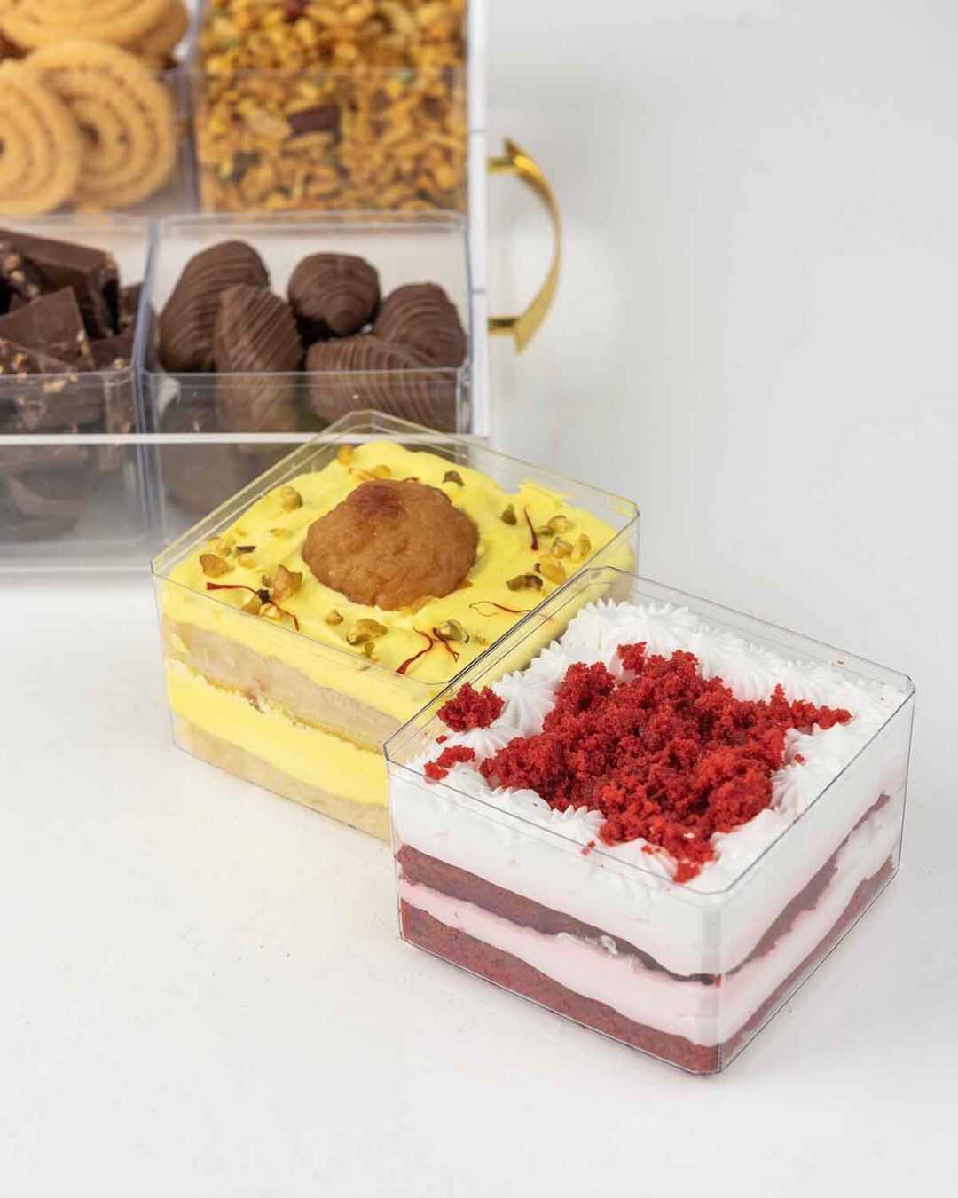 A transparent gift tray filled with assorted treats like cakes, truffles, and snacks for Diwali.
