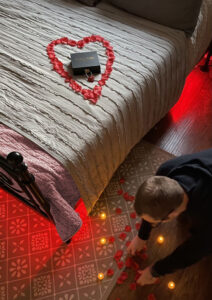 A Must-Have Valentine's Day Guide 2025: Everything You Need 5 A person decorating the room with rose petals for the scavenger hunt. A black box with a red lock is placed on the bed inside a heart shape formed with rose petals