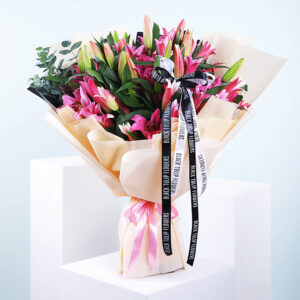 Top 10 Floral Arrangements to Honour Breast Cancer Awareness Month 3 A bouquet of pink lilies wrapped in beige paper with a pink ribbon and black ribbon accents.