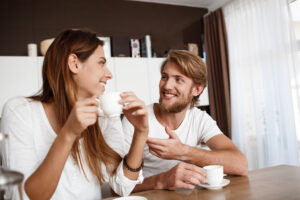 Valentine's Day Gift Ideas for Every Relationship ( 25 ideas) 3 A young, smiling couple sits at a kitchen table, enjoying their morning coffee