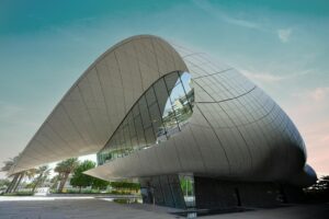 Top Ways to Celebrate UAE National Day with Family and Friends 5 A modern, white building with a unique, flowing design, reminiscent of a seashell. The building features large glass windows and a curved roof. Palm trees and a blue sky with clouds complete the scene.