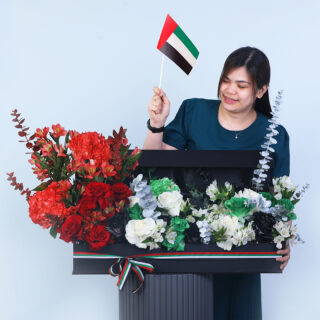 Hydrangeas, roses, alstroemerias, and eucalyptus arranged in a long rectangular box, tied with a UAE flag-coloured ribbon.