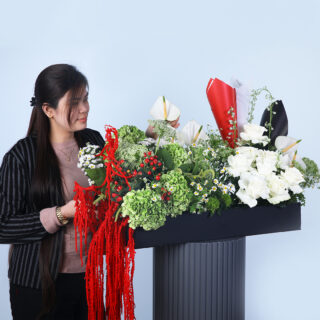 A black rectangular box filled with green hydrangeas, white roses, red amaranthus, and a mix of premium blooms in flag colours