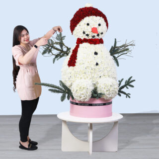 Snowman-shaped floral arrangement with white chrysanthemums, red roses, and nobilis leaves in a decorative box