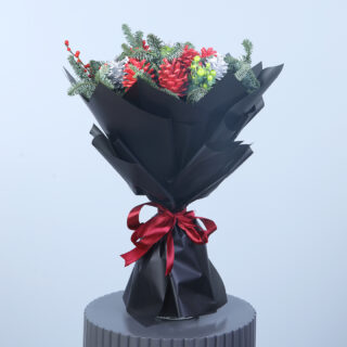 A winter bouquet with red accents, greenery, and pinecones, elegantly wrapped in black paper with a red ribbon on a modern stand