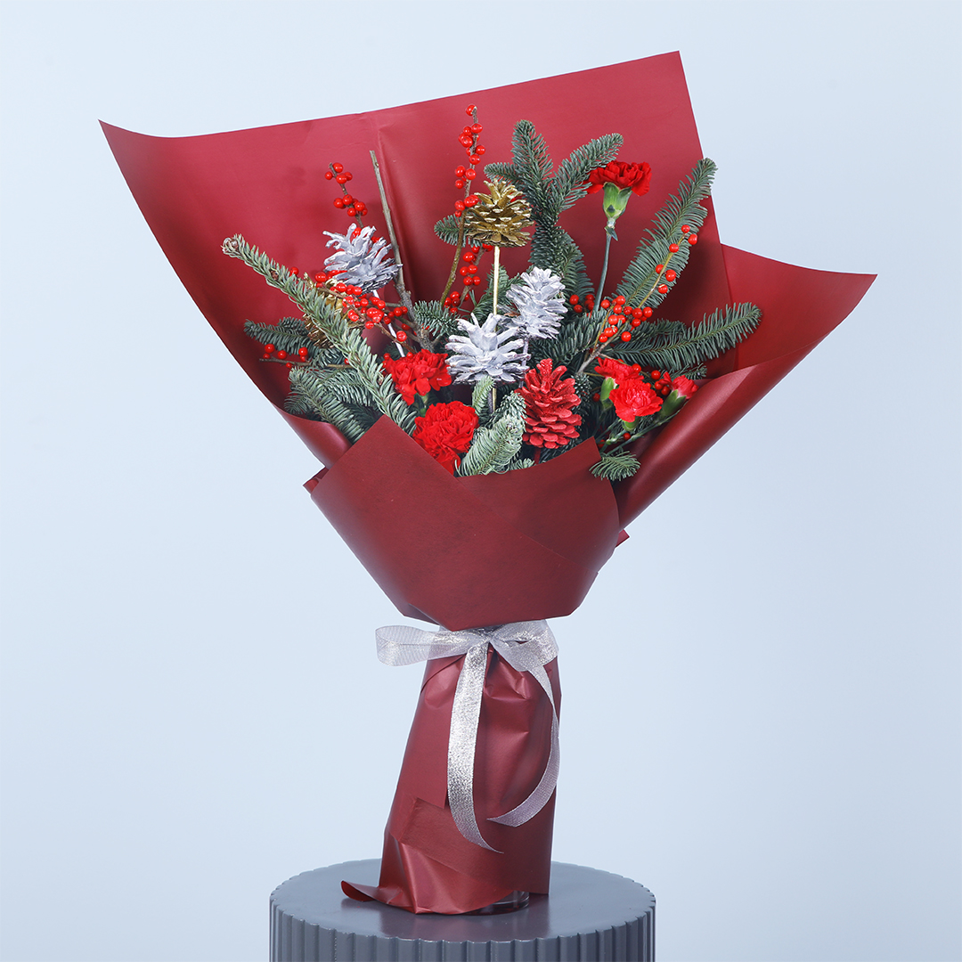 red_green_delight_bouquet Christmas bouquet with red flowers, silver pinecones, and greenery, wrapped in burgundy paper and a silver ribbon on a stand.