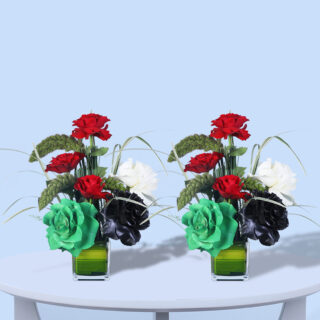 Floral arrangement with red, white, and black roses, accented by greenery and designed in a modern glass vase.