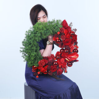 A vibrant red Christmas wreath with lush greenery, adorned with red ornaments, berries, and flowers.