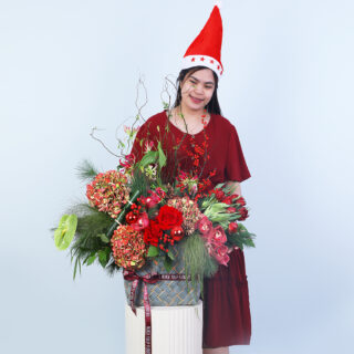 A vibrant Christmas floral basket featuring hydrangeas, red cymbidium, green anthurium, ilex berries, and lush greens.
