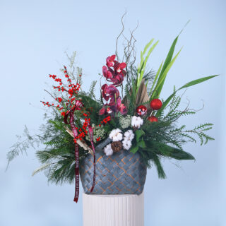 Elegant holiday arrangement with red roses, pinecones, berries, and festive accents in a basket. Perfect for decor.