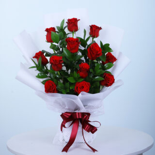 A bouquet of 12 red roses with leaves wrapped in white tied with a maroon ribbon.