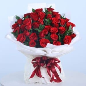 A lush bouquet of red roses wrapped in white paper with a dark red ribbon and bow.