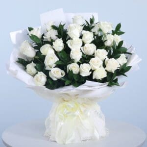 A bouquet of pristine white roses wrapped in white paper with a soft yellow ribbon.