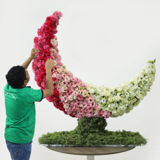 Crescent-shaped floral arrangement with red, pink, and white roses on a green moss base