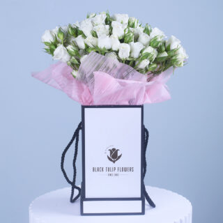 A bouquet of fresh white roses wrapped in pink paper, elegantly arranged in a Black Tulip Flowers branded gift bag.