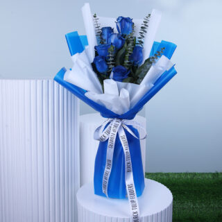 A bouquet of blue roses with eucalyptus wrapped in white and blue paper and tied with a white ribbon.