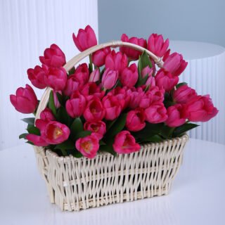 A woven basket filled with vibrant pink tulips, displayed on a white round table.