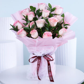 A beautiful bouquet featuring soft pink roses, hand-tied and wrapped in light pink, displayed on a white table.
