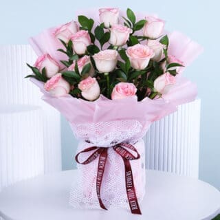 A beautiful bouquet featuring soft pink roses, hand-tied and wrapped in light pink, displayed on a white table.