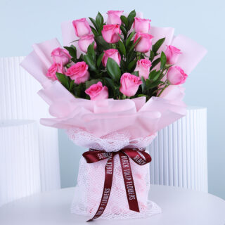 A delicate bouquet of soft pink roses, carefully arranged in light pink wrap, displayed on a white table.