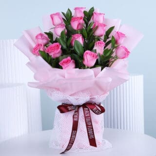 A delicate bouquet of soft pink roses, carefully arranged in light pink wrap, displayed on a white table.