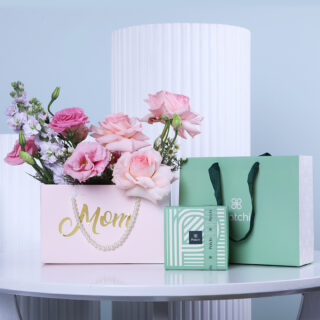 Pink and purple flowers in a 'Mom' bag, accompanied by a green box filled with Patchi chocolates and a green gift bag.