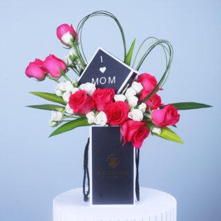 Floral arrangement with pink and white roses in a stylish black box, accented with a heart-shaped leaf design and an "I Love Mom" tag,