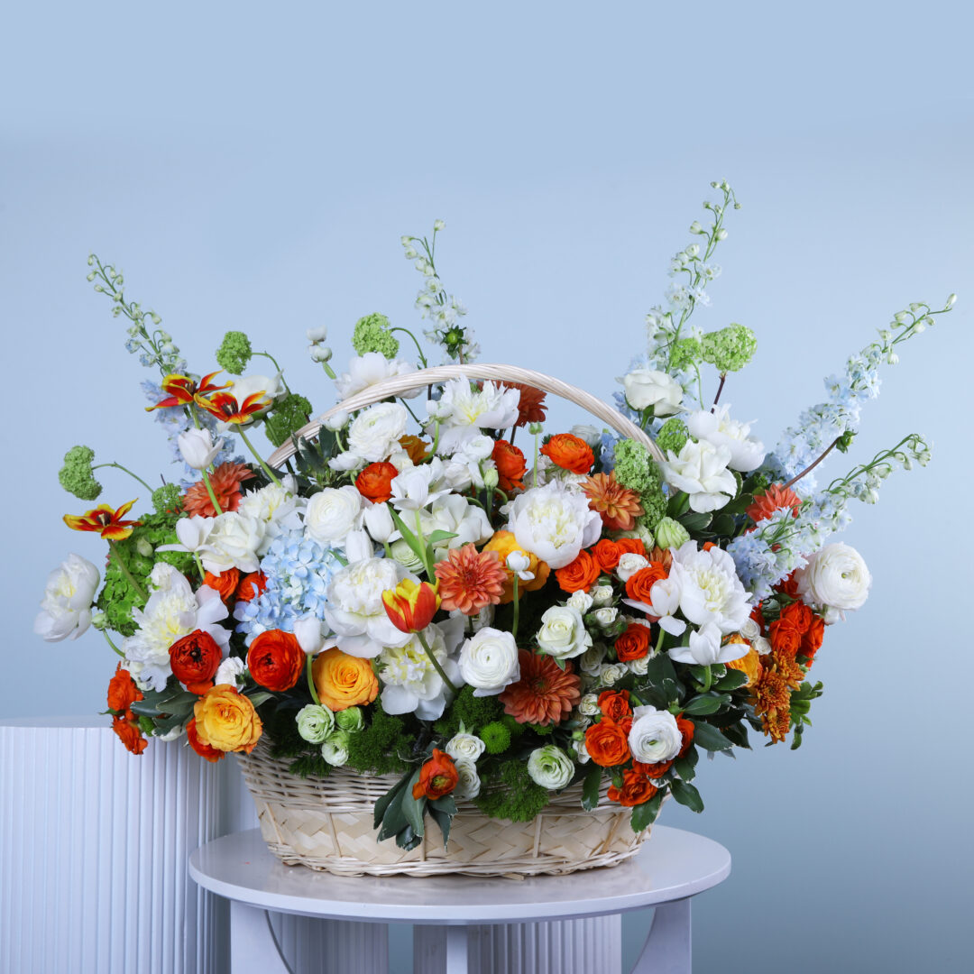 A large floral woven basket with handle filled with mixed flowers.